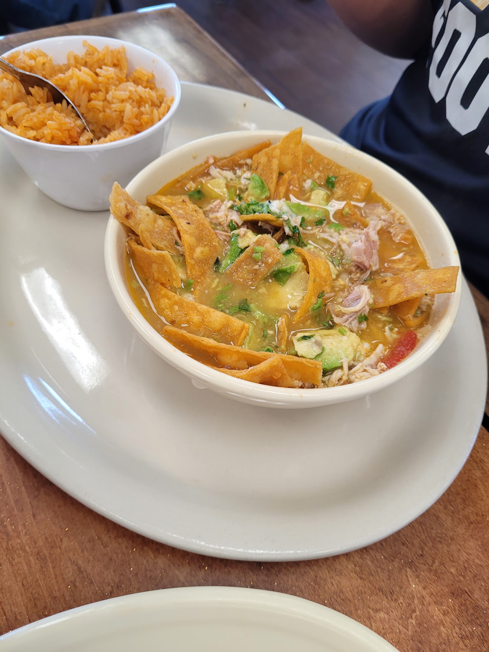 Tortilla soup topped with avocado, shredded chicken and crispy strips, served with rice